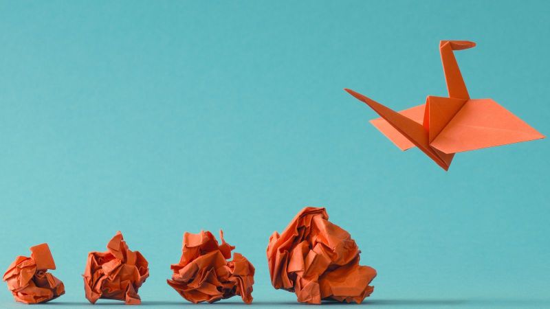 Das Bild zeigt vier größer werdende rote Papierknäuel und ganz rechts einen fliegenden Origami-Vogel.