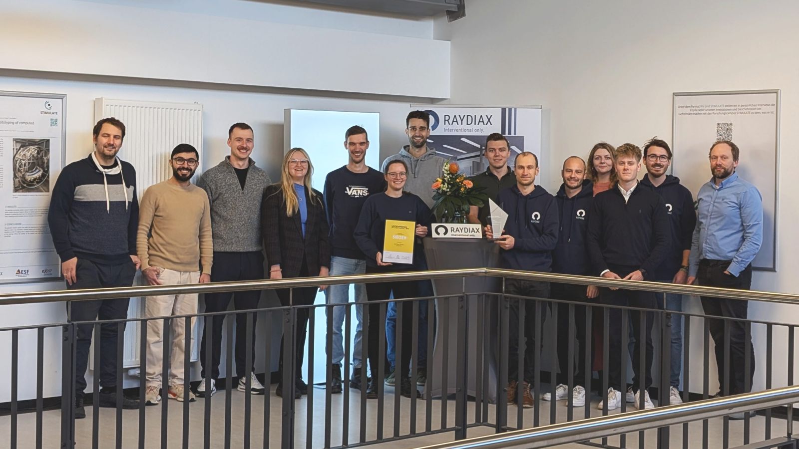 Die Gruppe postiert auf einer Galerie vor Posterwänden